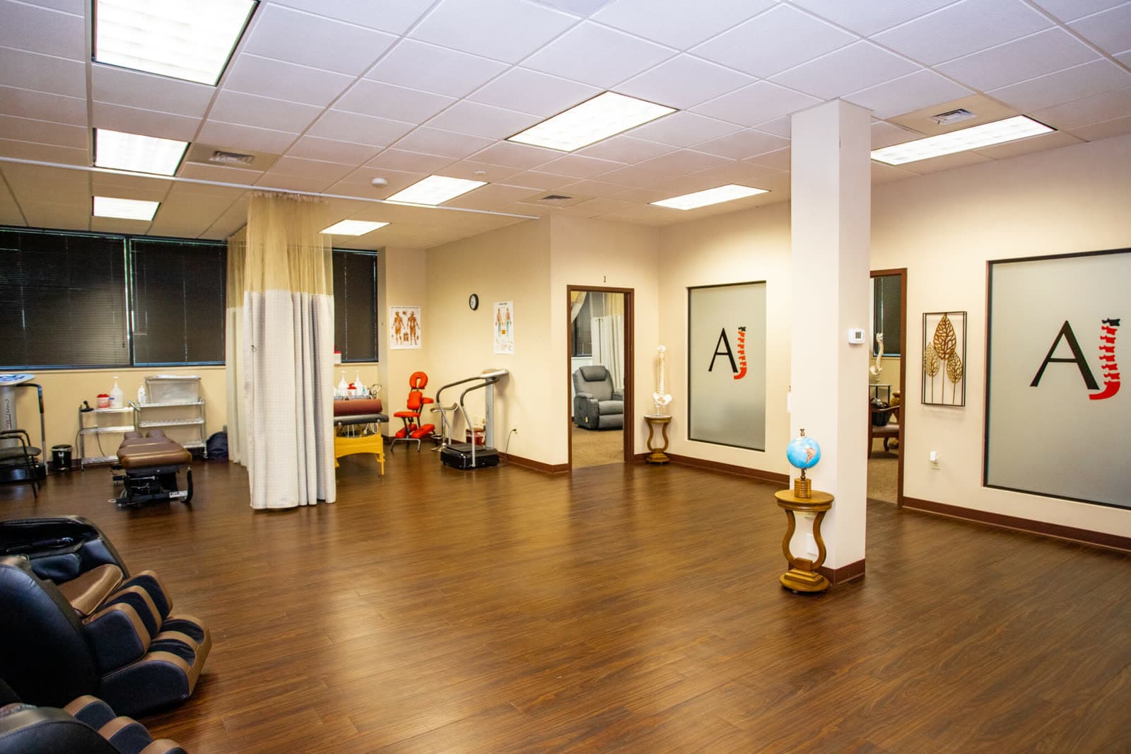 The open treatment floor at AJ Therapy Center: therapy tables, massage chairs, and the AJ mark on the wall